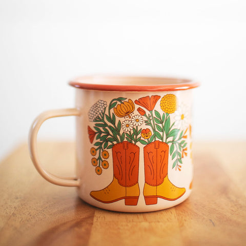 Western Bloom Enamel Mug 16oz with floral boot design by Trek Light on a wooden table, perfect for cozy sips.