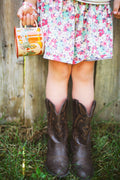 Western Bloom Enamel Mug 16oz in a child's hand, paired with brown cowboy boots and a floral dress.