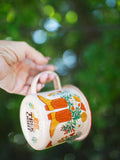 Hand holding Trek Light Western Bloom Enamel Mug 16oz with colorful floral design, perfect for outdoor adventures and happiness.