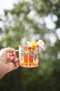 Western Bloom Enamel Mug 16oz with floral design and country boots, held outdoors with soft background blur.