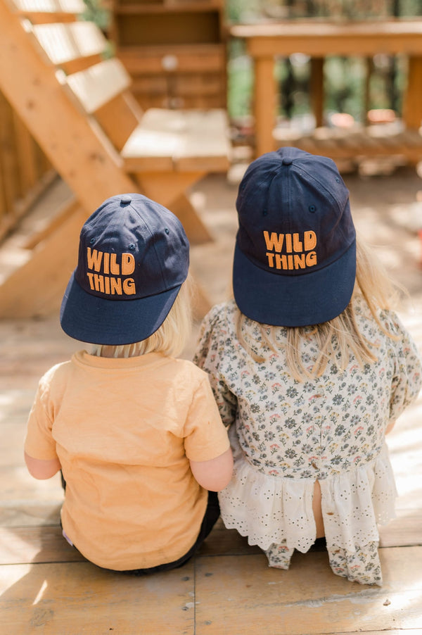 Two kids wearing Wild Thing Kids Hat, enjoying a sunny day of fun and adventure in the park.