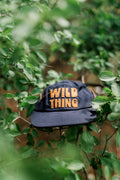 Wild Thing Kids Hat resting on green foliage, showcasing a playful design for adventurous children.