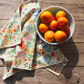 Wildflower Wonder Kitchen and Tea Towel with floral design next to a bowl of oranges on a wooden surface.