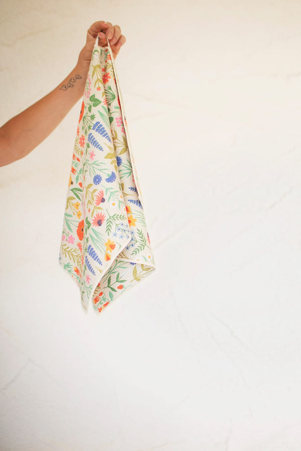 Wildflower Wonder Kitchen & Tea Towel featuring vibrant floral designs and a hand holding it for easy display.