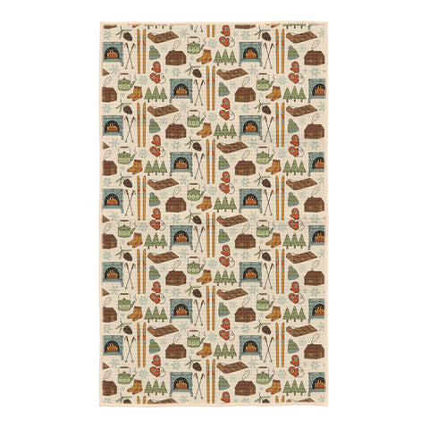 Winter Wonderland kitchen tea towel with illustrated cabins, wood stoves, skis, mittens, kettles and pine trees on cream
