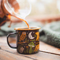 Trek Light Woodland Friends Enamel Mug 16oz with forest animal designs being filled with coffee on a cozy wooden table.