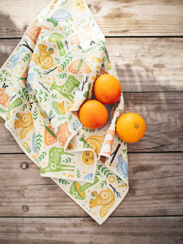 Woodland Friends Kitchen & Tea Towel with vibrant forest designs on wooden table with oranges, eco-friendly and super absorbent.