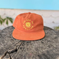 You Are My Sunshine Hat resting on a textured wooden surface, showcasing its vibrant orange color and cheerful design.