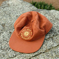 "You Are My Sunshine" hat in rust color on rock, part of matching hats set for kids and adults, perfect for Twinsie adventures. By Trek Light.