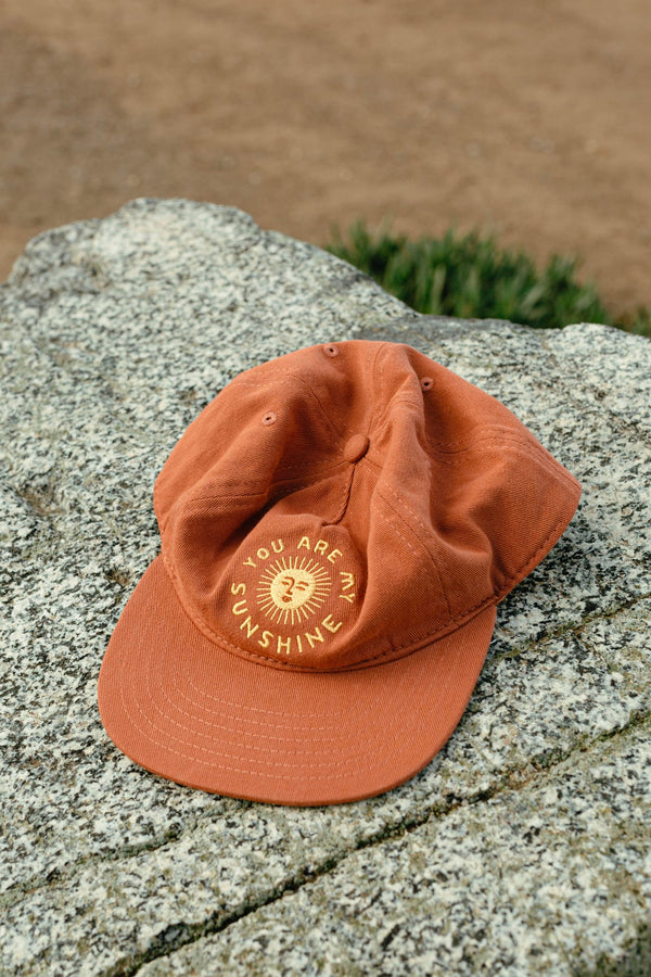 "You Are My Sunshine" snapback hat by Trek Light Gear on a rock, featuring sunny embroidery design for outdoor enthusiasts.