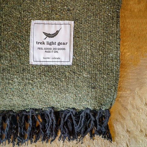 Close-up of a Humboldt Blanket by Trek Light Gear, showcasing woven texture and label. Made from recycled materials, supporting tree planting.