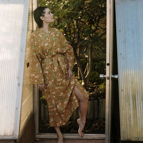 Person wearing cozy Agave Robe by Trek Light stands in a garden doorway, showcasing unisex fit and sustainable design.