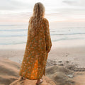 Person wearing an Agave Robe gazing at ocean waves, showcasing a cozy unisex fit by Trek Light against a serene beach scene.