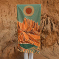 Trek Light towel with mountain and sun design held in front of rocky backdrop, blending nature and art for outdoor adventures.