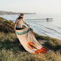 Person enjoying a cozy, versatile Arizona Blanket by the seaside; handwoven, made from recycled clothing materials, beautiful Trek Light design.