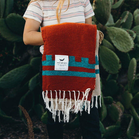 Handwoven Arizona Blanket made from recycled clothing, beautiful and cozy, perfect for versatile use by Trek Light, held in cactus backdrop.