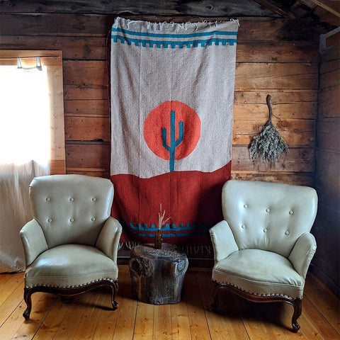 Arizona Blanket by Trek Light, handwoven from recycled clothing, draped in a cozy, rustic setting between two chairs. Beautiful and versatile design.