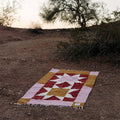 Beautiful handwoven Bernie Blanket made from recycled clothing, lying on desert ground, versatile and cozy. By Trek Light.