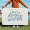 Person holding 'This Must Be The Place' canvas flag by Trek Light outdoors, showcasing artisanal hand-screened design and quality craftsmanship.