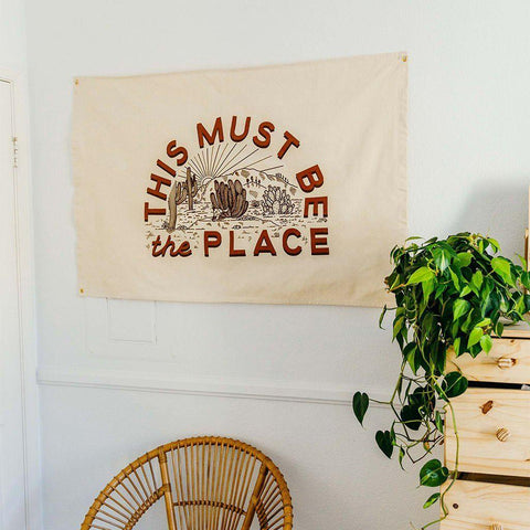 Trek Light's 'This Must Be The Place' canvas flag in a cozy room, featuring natural cotton and brass grommets for easy hanging.