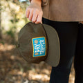 Alt Tag: Person holding Trek Light Day Tripper Snapback Hat with colorful logo and flat brim, perfect for outdoor adventures.