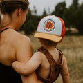 Child wearing a Trek Light Earth Day Kids Hat with an adult in a scenic outdoor setting, promoting outdoor adventure and sustainability.