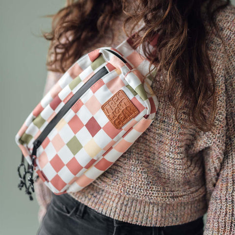 Person wearing Trek Light Everyday Fanny Pack in checkers, convertible from hip pack to shoulder sling, versatile and stylish bag.