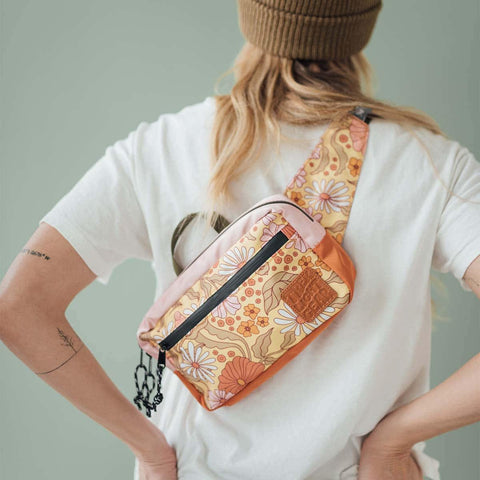 Model wearing Trek Light Everyday Fanny Pack in Bloom design, styled as a shoulder sling over white shirt and beanie.