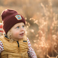 Adorable child wearing a Flower Child Kids Beanie by Trek Light, enjoying an outdoor adventure in autumn.