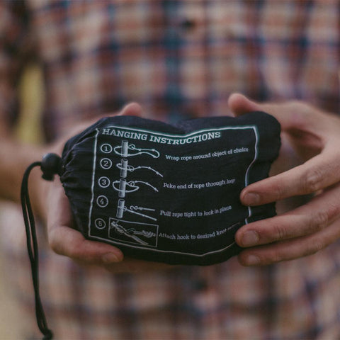 Alt Tag: Person holding Trek Light Go Anywhere Rope Kit with hanging instructions printed on the pouch, perfect for on-the-go hammocking.