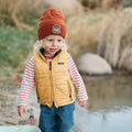 Child near water wearing a Good Vibes Kids Beanie by Trek Light, spreading positivity and charm in a cozy outdoor setting.