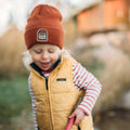 Happy child wearing a Good Vibes Kids Beanie by Trek Light, spreading joy with a smile and cozy style.