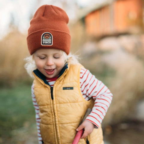 Happy child wearing a Good Vibes Kids Beanie by Trek Light, spreading joy with a smile and cozy style.