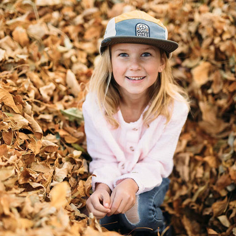 Child wearing Good Vibes Kids Hat by Trek Light smiles in autumn leaves.