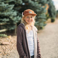 Girl wearing Good Vibes Sherpa Kids Hat by Trek Light, smiling in outdoor setting, styled with glasses and cozy jacket.