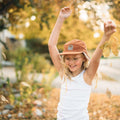 Smiling child wearing a Good Vibes Sherpa Kids Hat in fall scenery with leaves, featuring Trek Light style. Ideal for ages up to 3-4+.