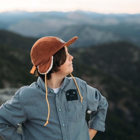 Child wearing Good Vibes Sherpa Kids Hat by Trek Light, outdoors in nature, showcasing stylish 5-panel corduroy snapback with flaps.