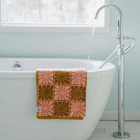 Groovy Flowers Bath Towel by Trek Light, sustainably made from 100% cotton, draped over a tub for a cozy and stylish bath experience.