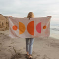 Person holding Half Moon Wander Towel on beach. Sustainable, made with recycled materials. Trek Light, quick-dry, super absorbent.