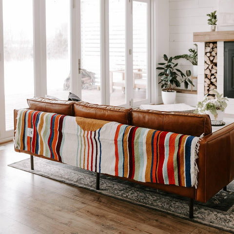 Vibrant Halley's Comet Blanket by Trek Light draped over a cozy brown leather sofa in a well-lit, stylish living room.