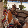 Cozy setting with a woman and a vibrant Halley's Comet blanket by Trek Light, surrounded by plants in a rustic space.