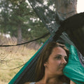 Woman relaxing in hammock with Bug & Rain Hammock Accessory Kit by Trek Light, enjoying nature's tranquility.