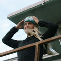 Woman in a black jacket smiling and wearing the Happiest Camper Tie Dye Beanie by Trek Light on a breezy day.