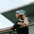 Person wearing Happiest Camper Tie Dye Beanie by Trek Light, standing outside with wind-blown hair, enjoying the outdoor view.