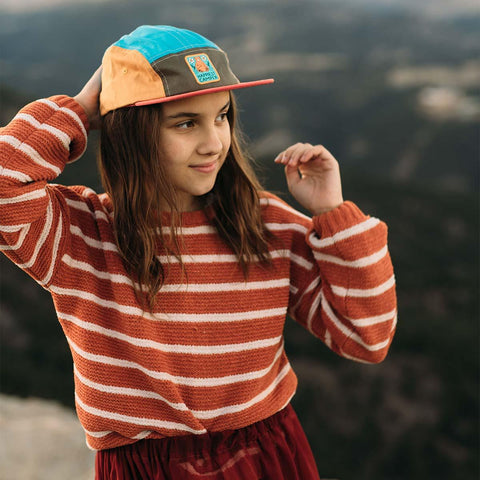 Child wearing Happiest Camper Kids Hat by Trek Light, 5-panel snapback, flat brim, colorful design, outdoors adventure spirit.