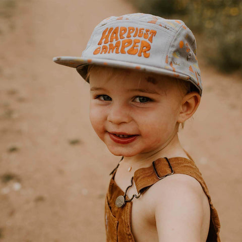 Smiling child wearing the Happiest Camper Kids Hat by Trek Light on a nature trail, perfect for outdoor adventures and fun.
