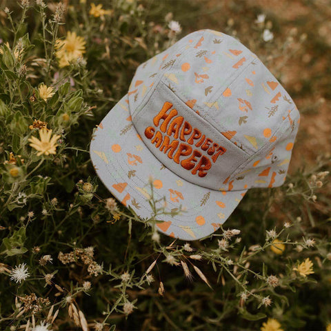 Trek Light Happiest Camper Kids Hat with vibrant print, nestled in wildflowers, perfect for outdoor adventures.