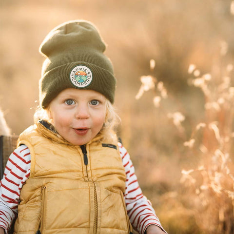 Adorable child wearing Happiest Camper Kids Beanie by Trek Light in a scenic outdoors setting, showcasing joyful adventure vibes.