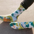 Bright tie dye socks with smiley face and 'Happiest Camper' design, perfect for comfort and adventure. Trek Light quality.