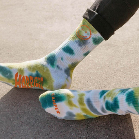 Bright tie dye socks with smiley face and 'Happiest Camper' design, perfect for comfort and adventure. Trek Light quality.